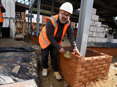 Image by Vikki Lince - a man in a hard hat and high vis jacket has laid a brick for the new Grove Cottage building