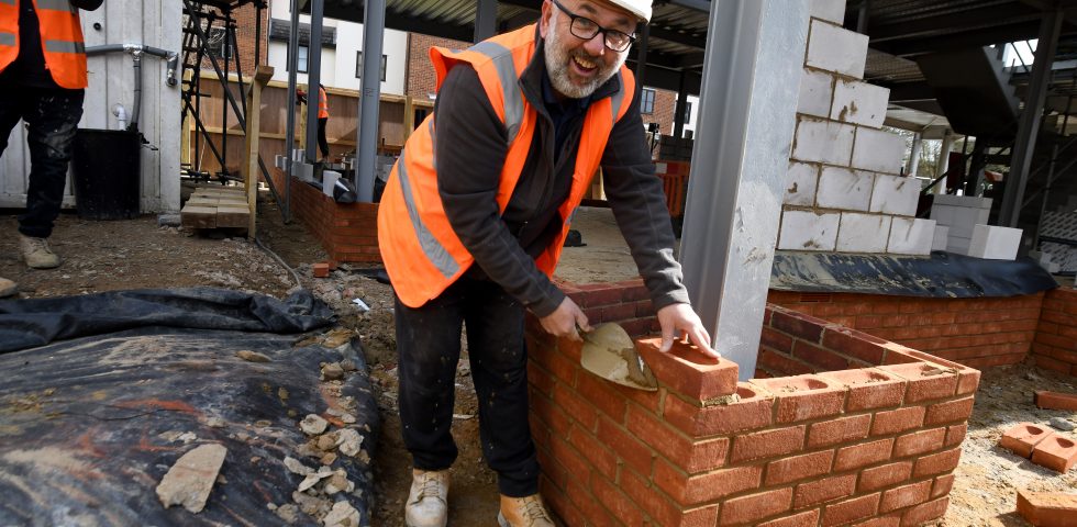 Image by Vikki Lince - a man in a hard hat and high vis jacket has laid a brick for the new Grove Cottage building